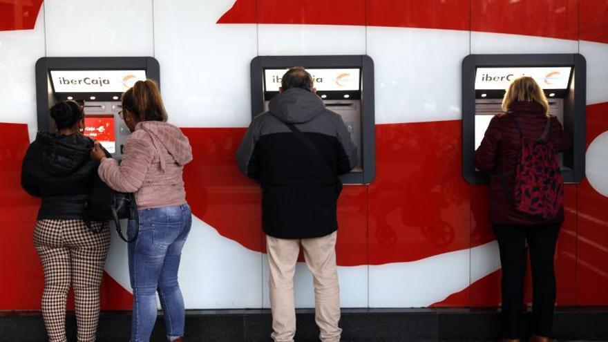 Varias personas sacando dinero esta semana en cajeros automáticos de Ibercaja situados en el centro de la ciudad de Zaragoza.  | MIGUEL ÁNGEL GRACIA