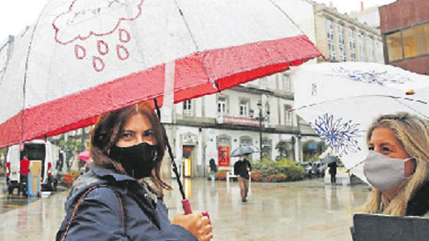 Dos mujeres con mascarilla conversan bajo la lluvia.