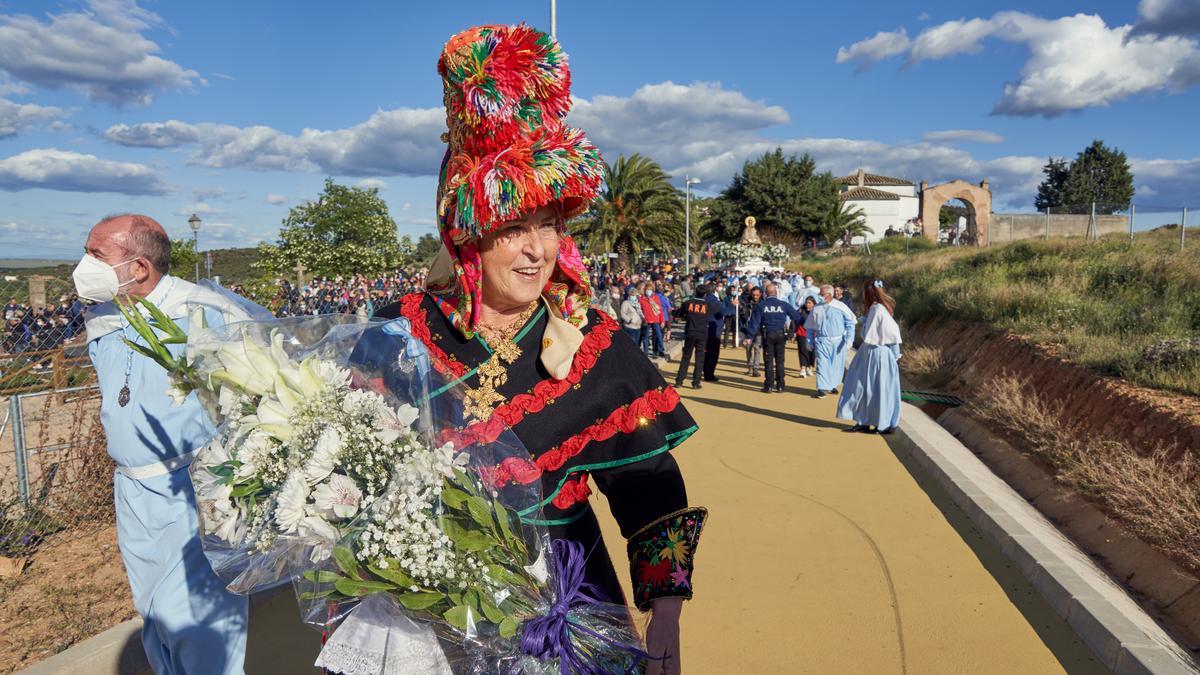 Una cacereña con el traje regional con un ramo de flores para la Virgen de la Montaña. Al fondo, la patrona antes de enfilar el puente de la Ronda Sureste.