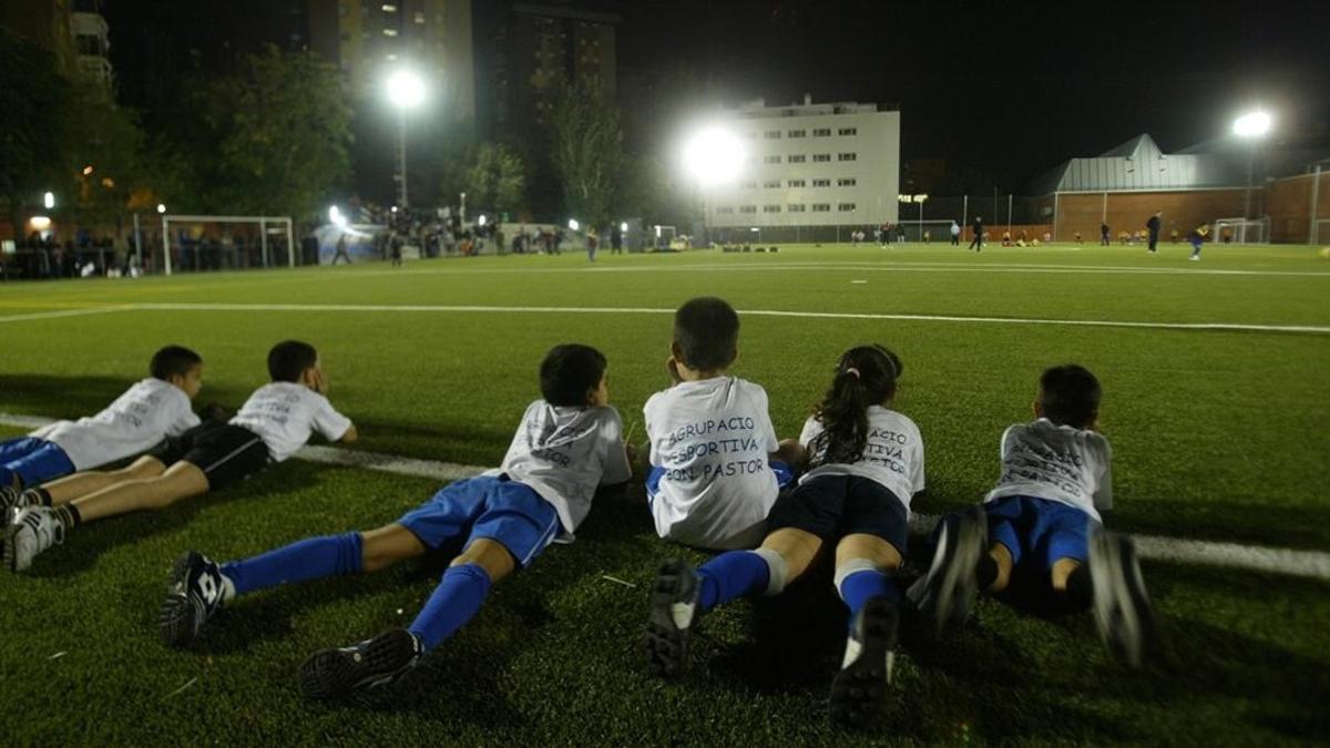Unos niños observan un partido en el campo de hierba artificial del Bon Pastor, en Barcelona.
