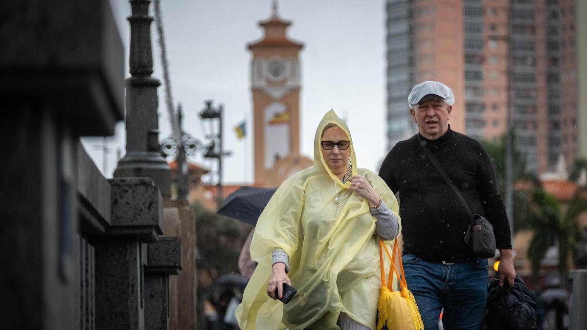Dos personas tratan de cubrirse de la lluvia con chubasqueros por el centro de Santa Cruz.