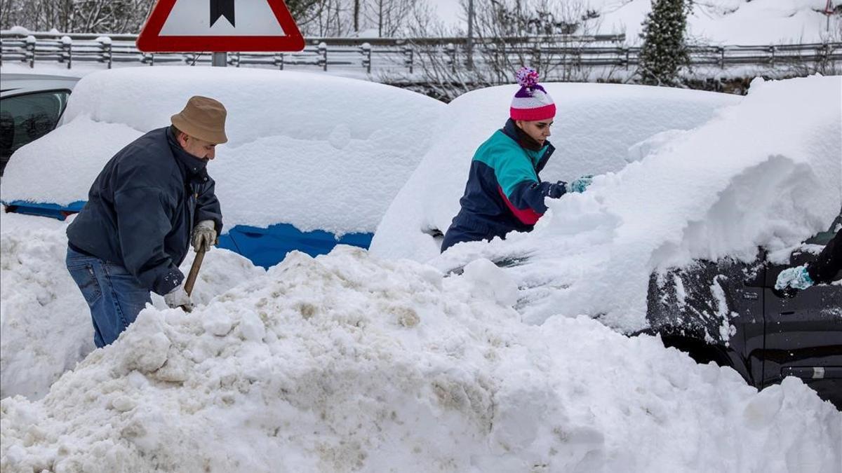 Unos vecinos quitan nieve de sus coches en el pueblo de Pajares