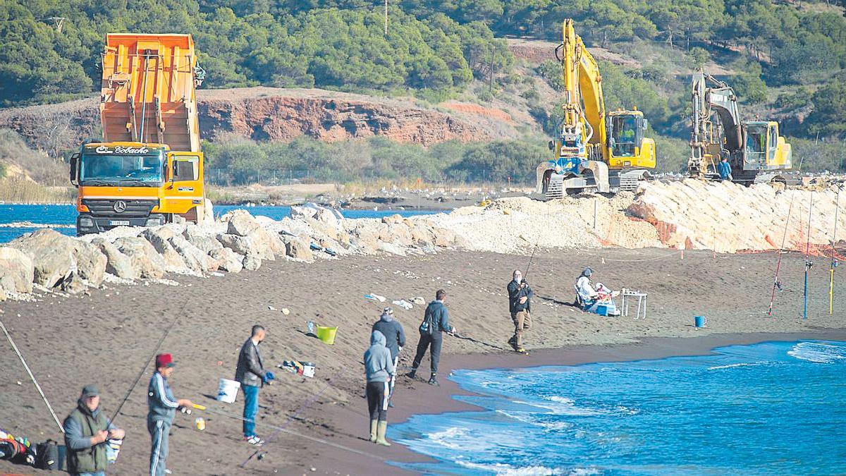 Varias máquinas afianzan la mota de la bahía frente a varios pescadores.