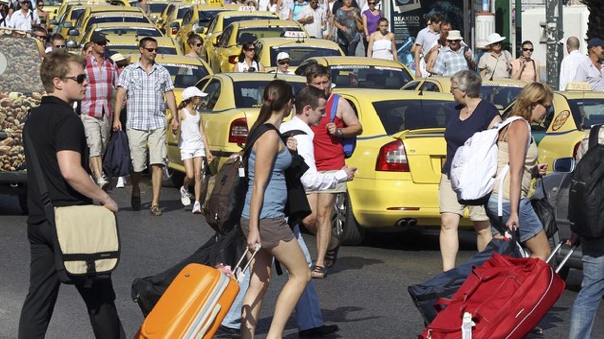 Varios viajeros pasan junto a los taxis aparcados que bloquean el acceso al puerto del Pireo.