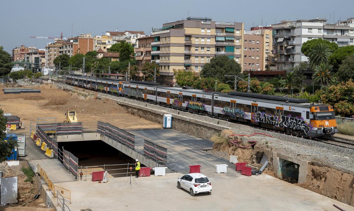 Un tren de Rodalies de la R4 pasa junto a las obras cerca de la estación de Sant Feliu de Llobregat donde se está trabajando para soterrar las vías del tren a su paso por el centro de la localidad.
