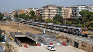 Un tren de Rodalies de la R4 pasa junto a las obras cerca de la estación de Sant Feliu de Llobregat donde se está trabajando para soterrar las vías del tren a su paso por el centro de la localidad.