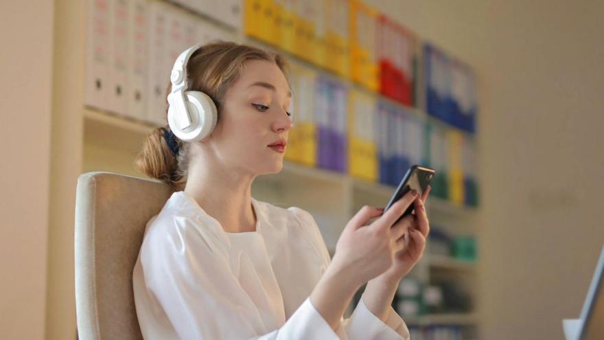 Una joven mira el móvil mientras escucha música. | Pexels