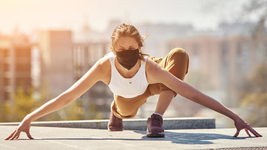 Una mujer hace yoga con mascarilla.