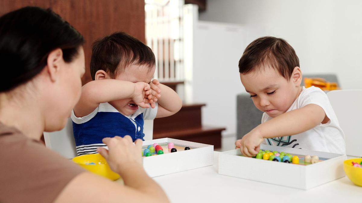 Un niño llorando mientras su hermano juega.
