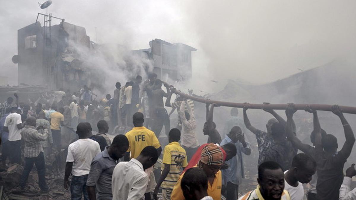 Varios ciudadanos ayudan a sostener una manguera para apagar las llamas del avión siniestrado, el domingo, en un barrio residencial de Lagos (Nigeria).