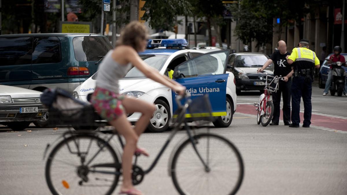 Una ciclista observa cómo un guardia urbano multa a una persona que va en bicicleta por saltarse un semáforo.