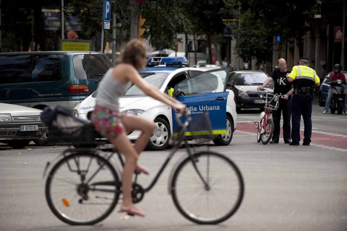 Una ciclista observa cómo un guardia urbano multa a una persona que va en bicicleta por saltarse un semáforo (Imagen de archivo).