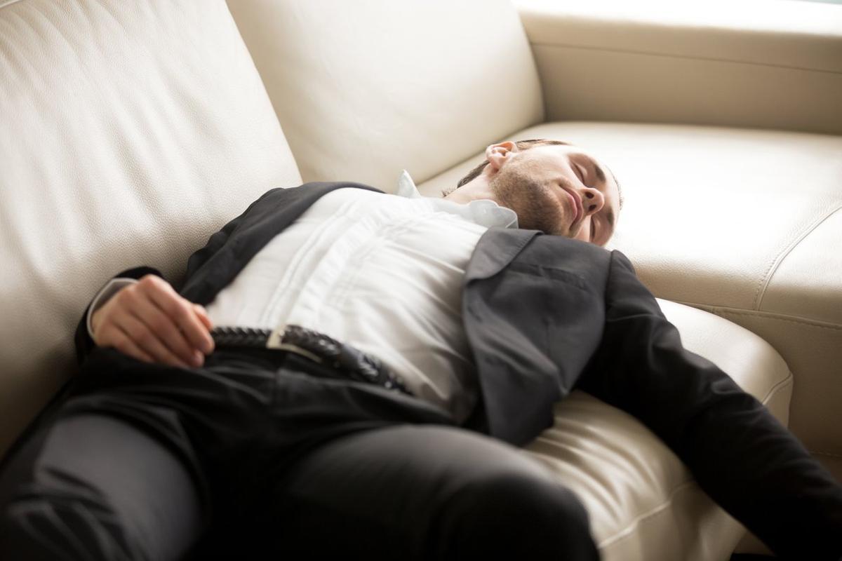 FOTO BAJADA DE 123RF EL 3 DE MAYO DEL 2019 PARA ILUSTRAR UN ARTICULO SOBRE CATAPLEXIA / NARCOLEPSIA. HOMBRE DORMIDO EN UN SOFA. DORMIR. DESCANSAR. DESMAYO. DESMAYADO. SIESTA. Close up of exhausted businessman laying on the couch. Young hard working entrepreneur fell asleep on sofa at workplace. Staying at work overtime, overworked, too much workload, lack of sleep concept. FOTO DE Aleksandr Davydov / 123 RF