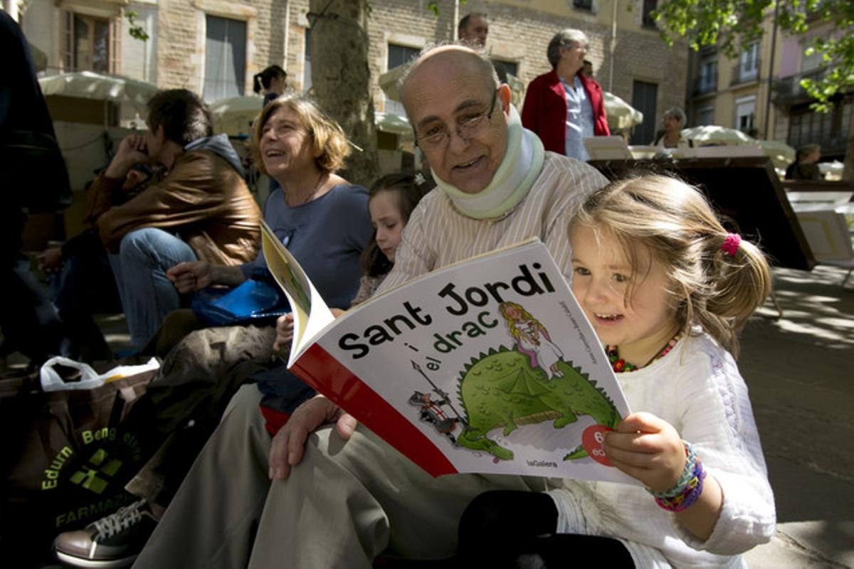 Una nena llegeix un llibre sobre la llegenda de Sant Jordi en companyia del seu avi.
