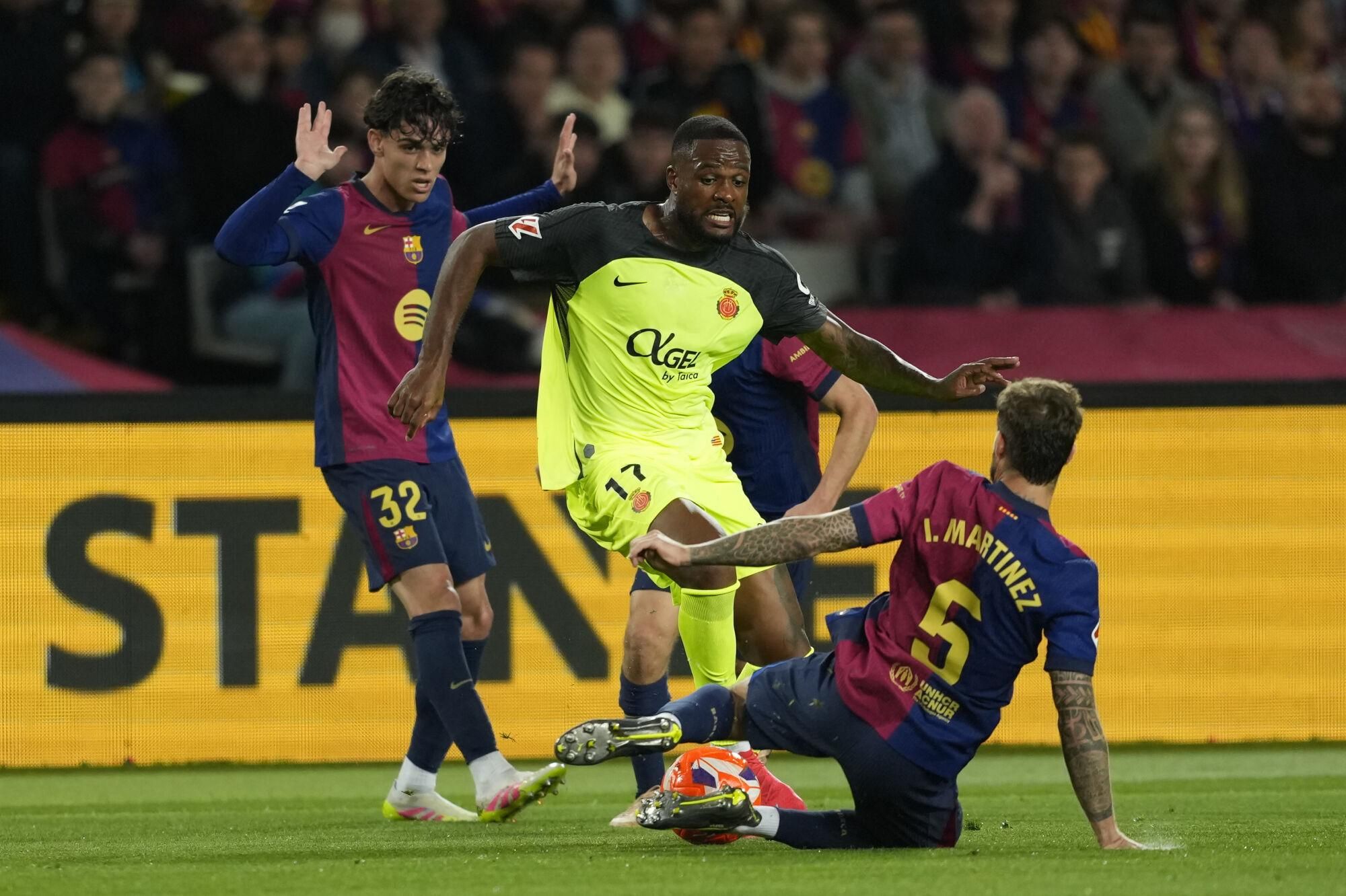 BARCELONA, 22/04/2025.- El delantero del Mallorca Cyle Larin (c) juega un balón entre Héctor Fort (i) e Íñigo Martínez, ambos del Barcelona, durante el partido de la jornada 33 de LaLiga que FC Barcelona y RCD Mallorca disputan hoy martes en el Estadi Olímpic Lluís Companys. EFE/Alejandro García