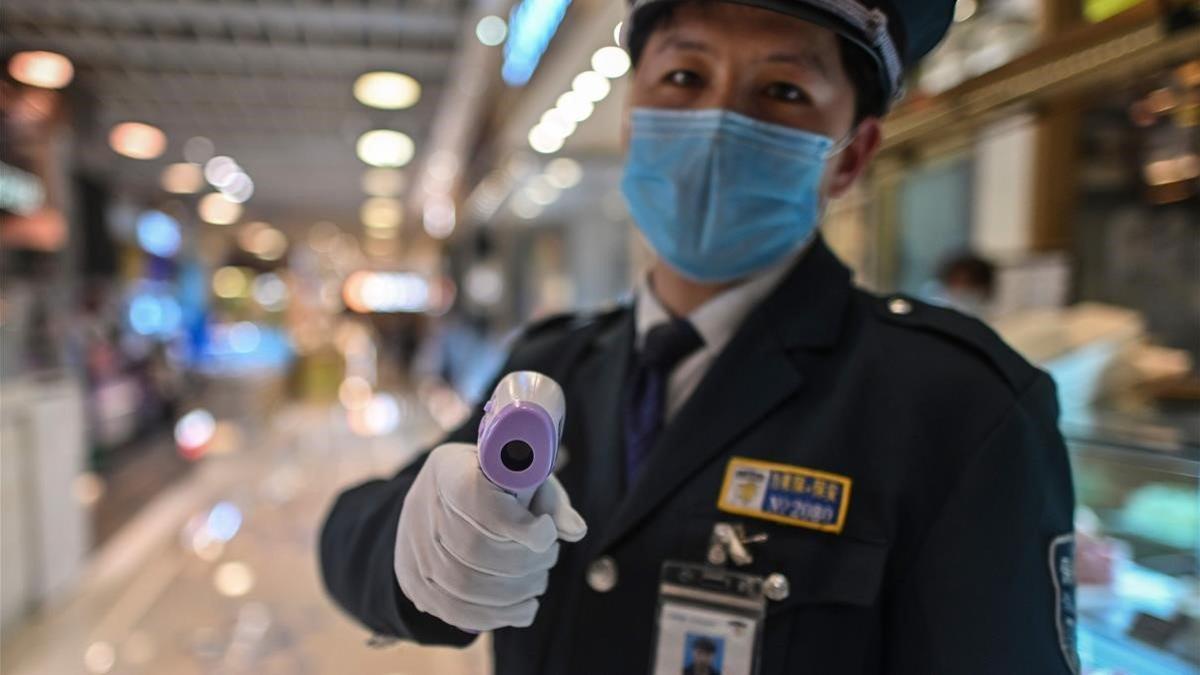 Un agente de seguridad mide la temperatura de los clientes de una zona gastronómica en Shanghái.