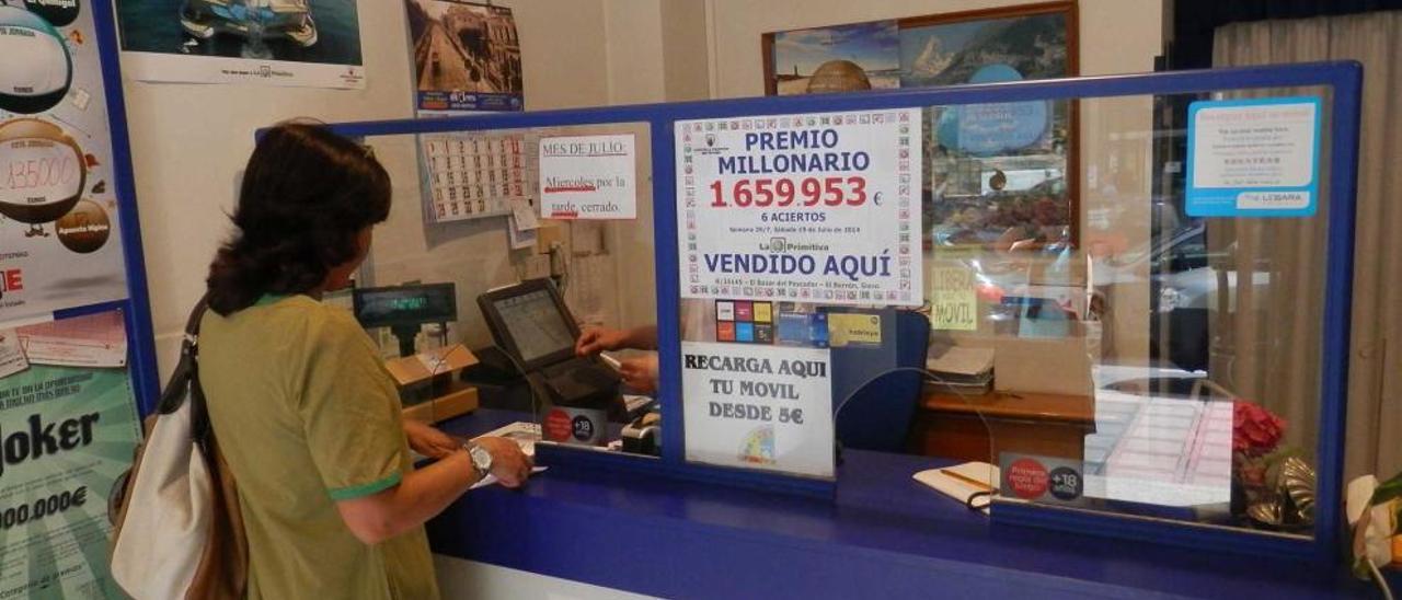 Una clienta compra lotería en la administración de El Berrón, donce luce el cartel con el premio.