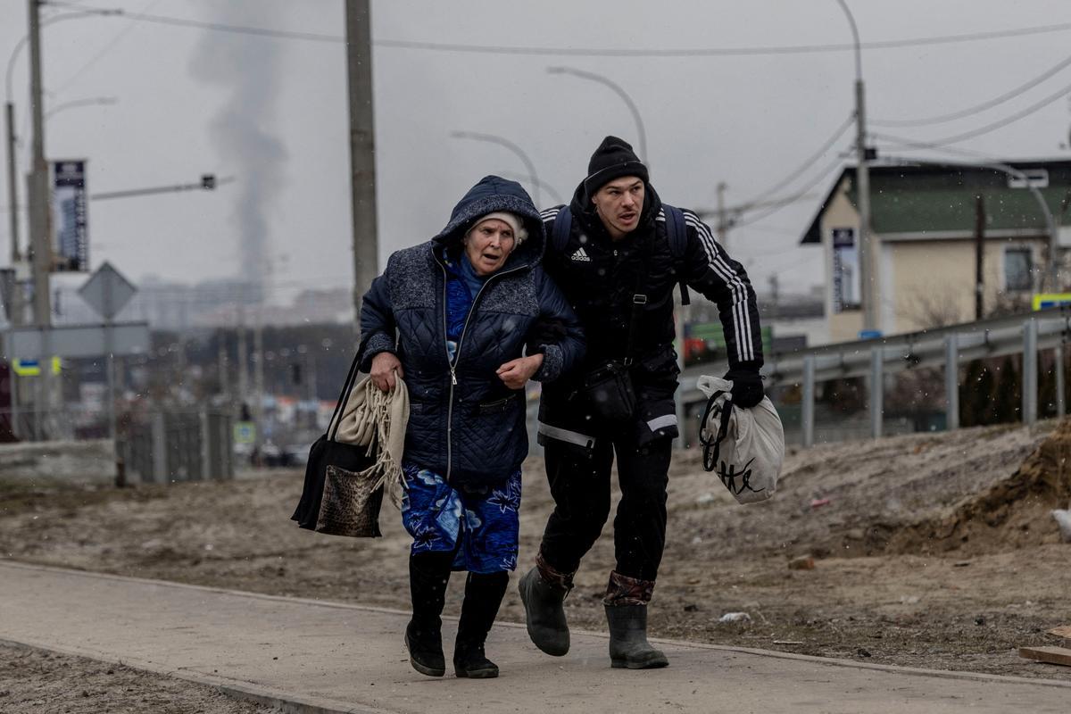 Un hombre ayuda a una mujer mayor a refugiarse a toda velocidad ante los bombardeos que caen en la ciudad ucraniana de Irpin.