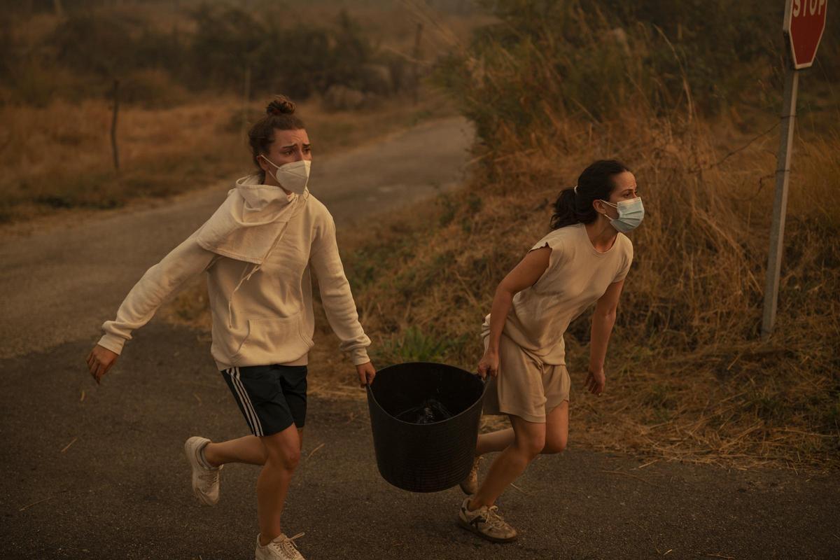 Dos mujeres corren con un cubo de agua para ayudar a combatir un incendio forestal en Carballeda de Avia. Ourense, Galicia, España, 17 de agosto de 2025.