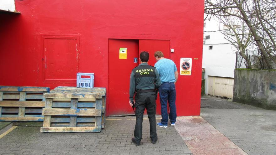 Un agente de la Benemérita y un vecino observando los daños en la puerta de hierro por la que accedieron los rateros al interior del supermercado