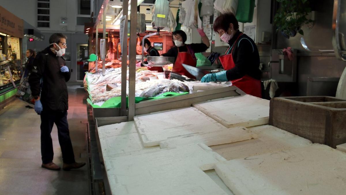 En primer término, una pescadería cerrada del Mercat del Lleó y, al fondo, pescaderías atendiendo a un cliente.