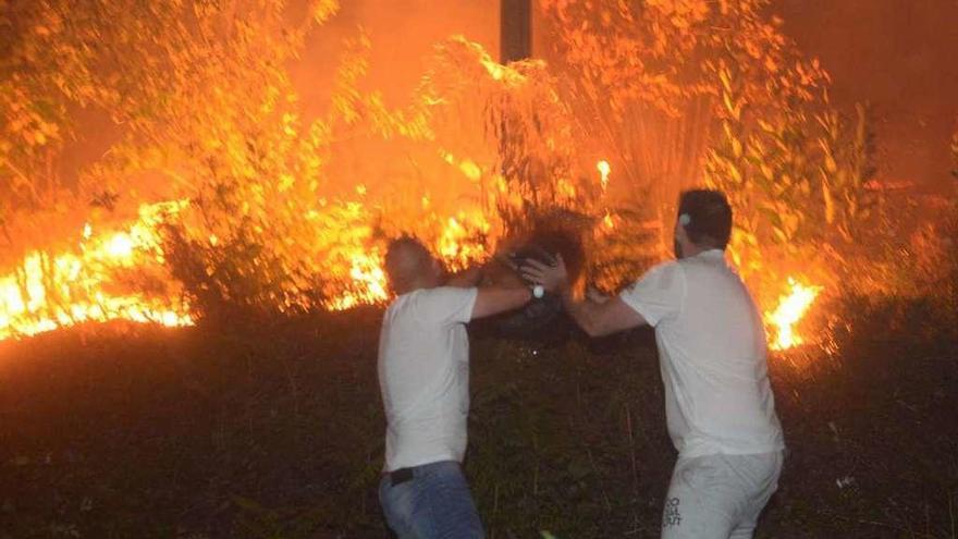 Dos hombres arrojan agua al fuego en As Pereiras, en la noche del domingo pasado. // Noé Parga
