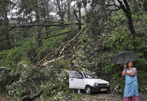 Una mujer se encuentra cerca de un coche que fue dañado por un árbol que cayó tras las fuertes lluvias y vientos en el norte de la ciudad india de Shimla.
