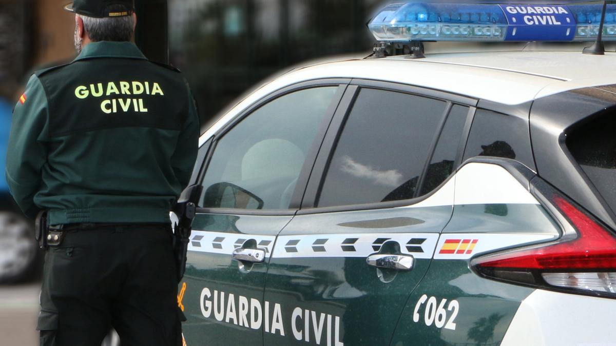 Un agente de la Guardia Civil, de espaldas, de pie junto a un vehículo oficial