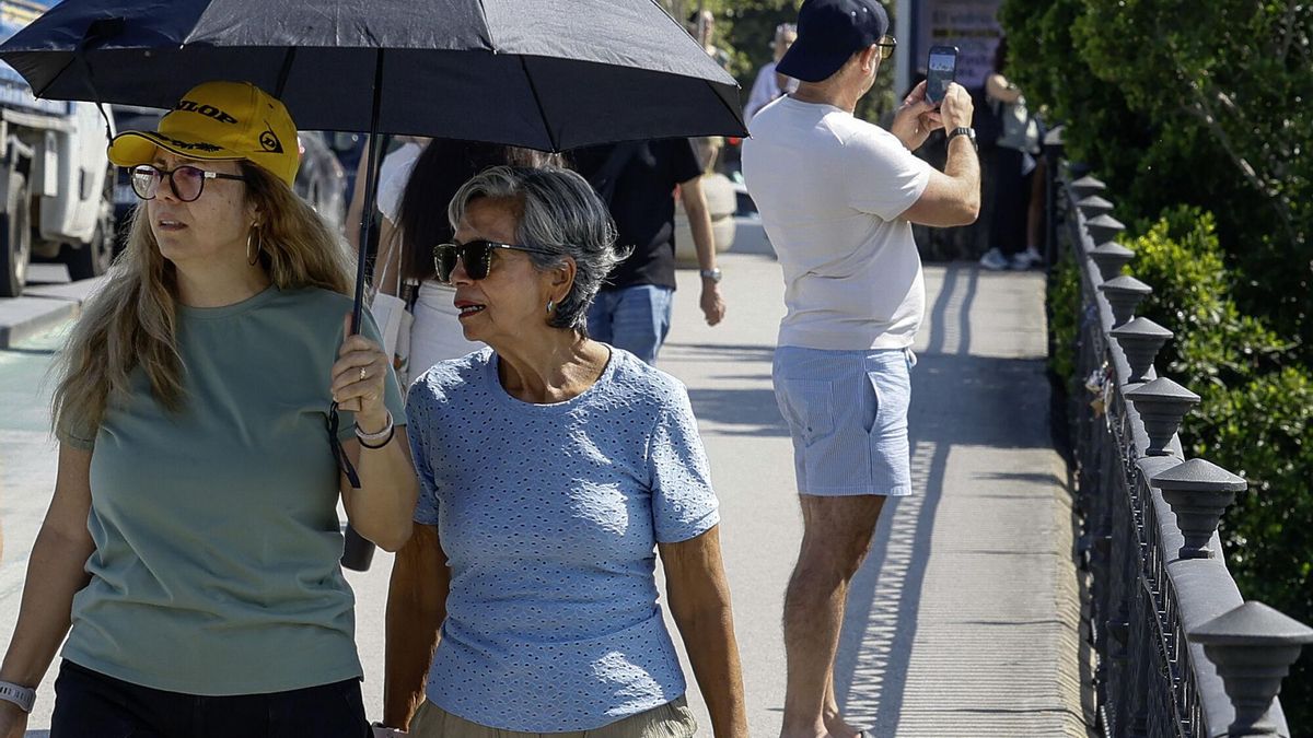 Varias personas se cubren del sol mientras caminan por el Puente del Triana de Sevilla.