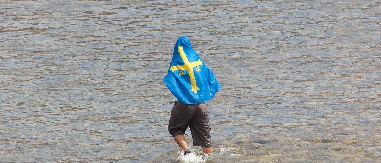 Un joven usa una bandera de Asturias para cubrirse en medio del Sella.