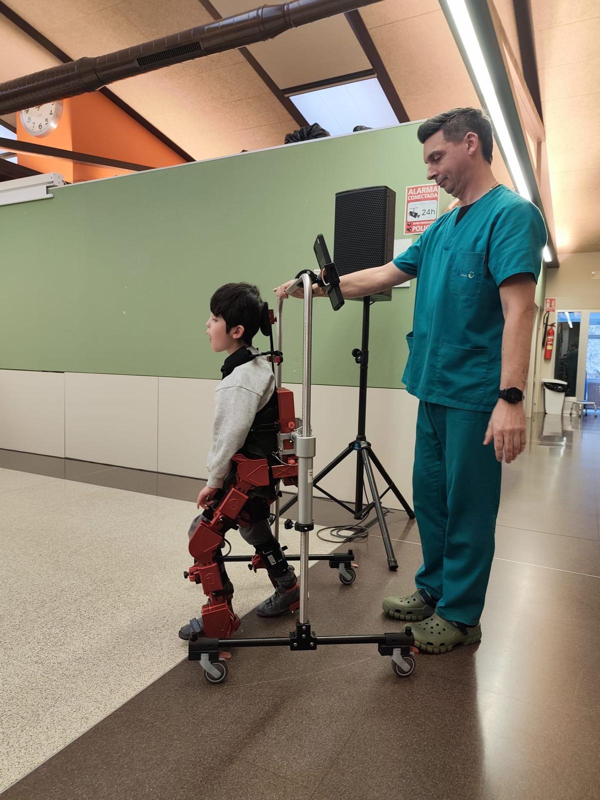 El pequeño Darío da unos pasos asistidos con el exoesqueleto, con la ayuda del fisioterapeuta Santiago Carral, este miércoles, en las instalaciones de Aspace Coruña.