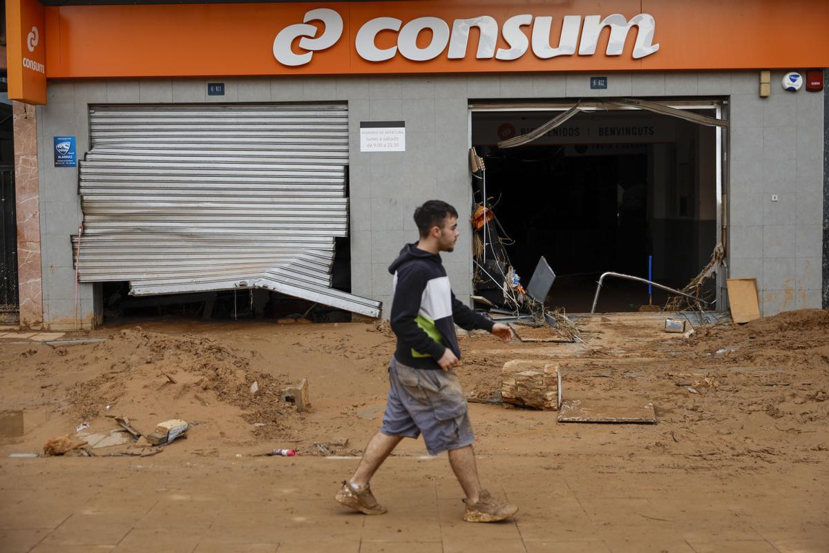 Un vecino camina junto a un comercio afectado en Paiporta.