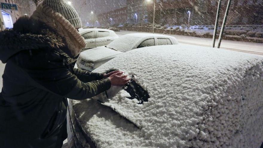 Una joven retira la nieve acumulada en su coche