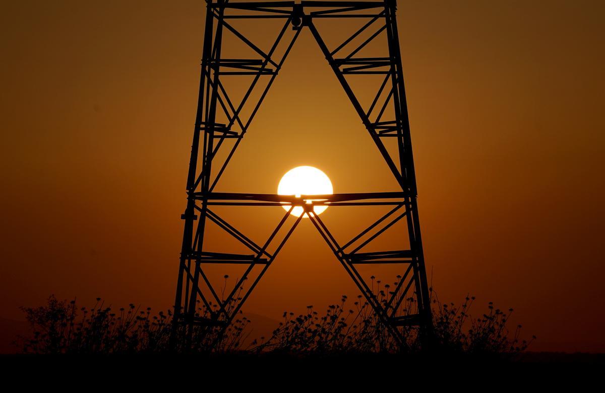 Una torre de electricidad con el sol de fondo.