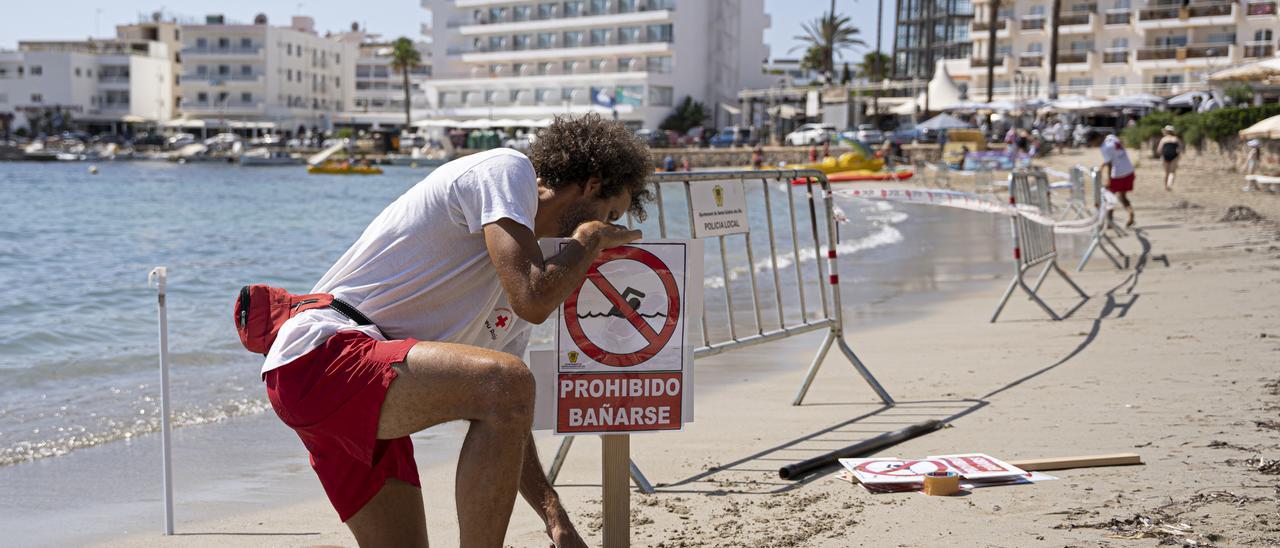 Un socorrista coloca el cartel de ‘Prohibido bañarse’ en la arena.