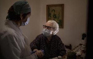 En tiempos de coronavirus, una cuidadora ayuda a una anciana a incorporarse en su piso de Barcelona.