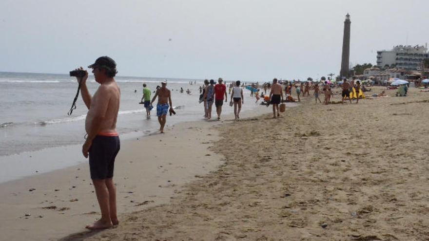 Un turista graba la marea desde la arena de la playa de Maspalomas, con el faro al fondo.