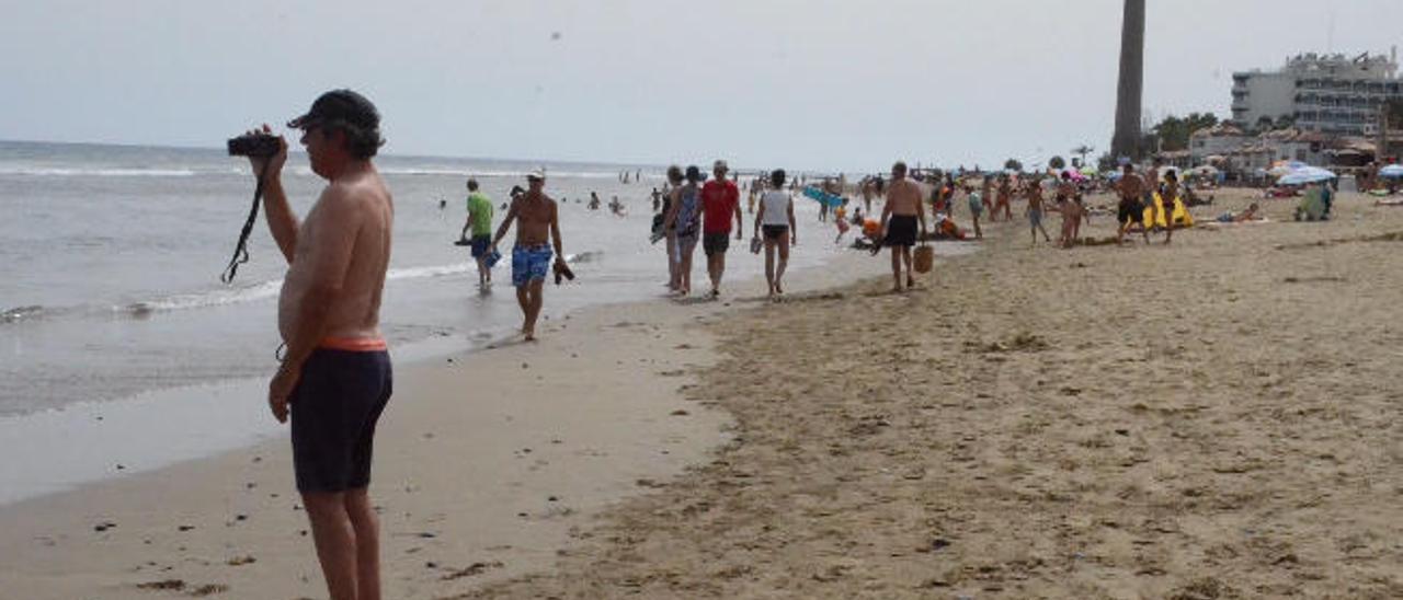 Un turista graba la marea desde la arena de la playa de Maspalomas, con el faro al fondo.