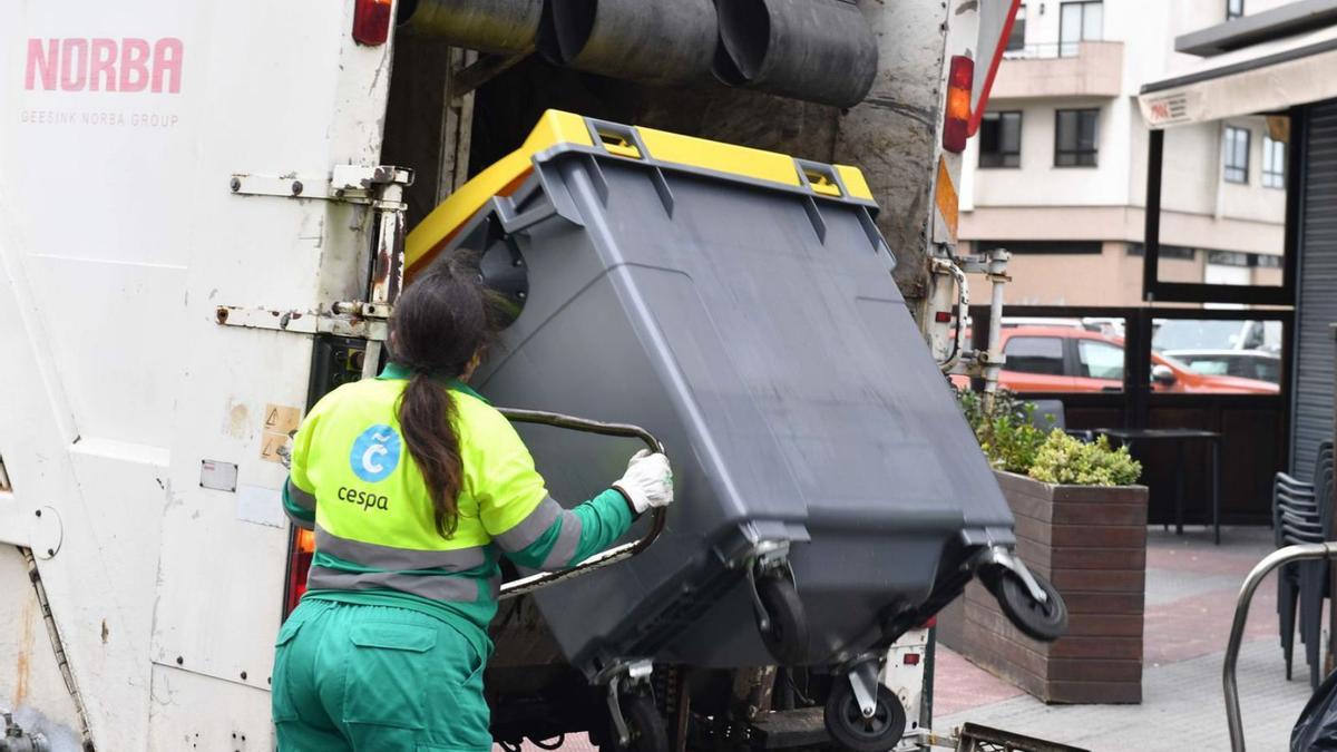 Una trabajadora de la recogida de la basura descarga un contenedor en un camión del servicio.