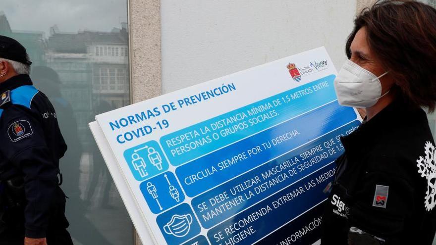 Una mujer transporta en Lugo varios carteles con normas de prevención del coronavirus.