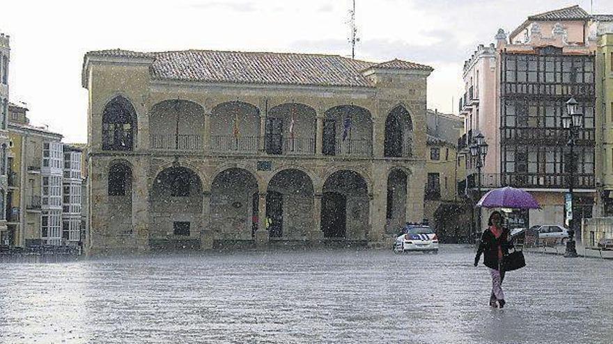 Una mujer se protege de las fuertes lluvias mientras camina por la Plaza Mayor de Zamora.