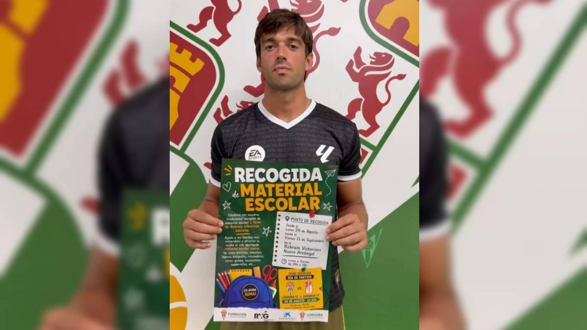 Iker Álvarez, jugador del Córdoba CF, sostiene el cartel de la cuarta Recogida de Material Escolar blanquiverde.