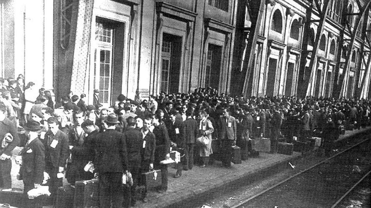 Trabajadores españoles con sus modestos equipajes, integrantes de una expedición oficial, agrupados en el andén de la estación.