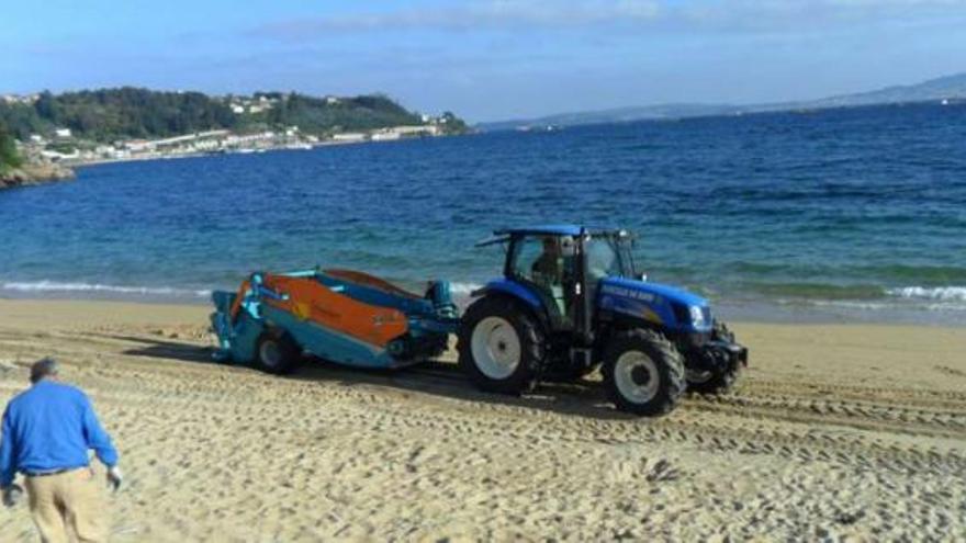 El tractor y la nueva máquina limpiaplayas trabajando en la playa de Banda do Río, en Bueu.  // FC