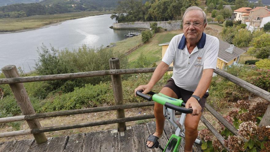 Sandalio Fernández, haciendo bici en el mirador de delante de su casa en El Castillo, con el pueblo, la fortaleza de San Martín y el río Nalón a su espalda. | | MIKI LÓPEZ