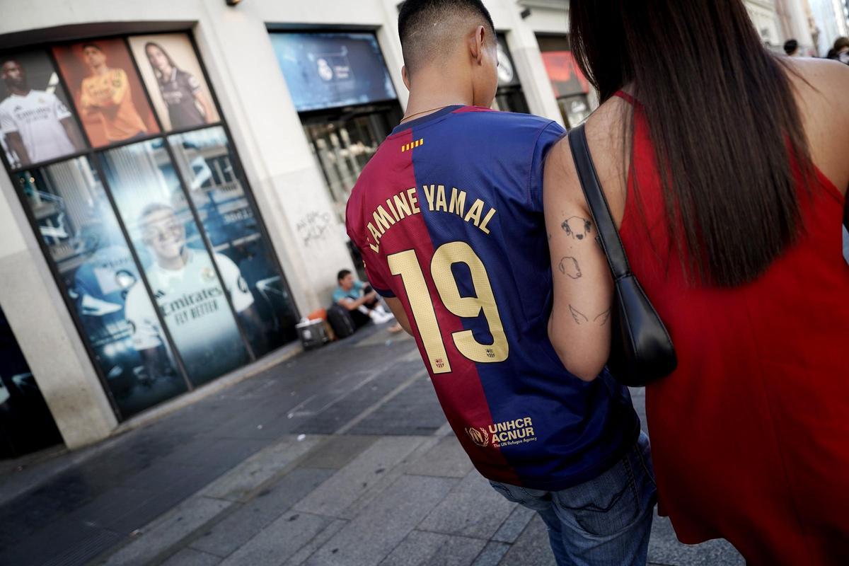 Un joven pasa en la Gran Vía madrileña ante el escaparate de la tienda oficial del Real Madrid con una camiseta falsificada de Lamine Yamal, del FC Barcelona.