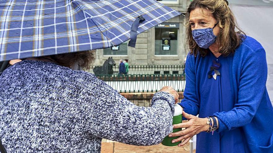 Una vecina donando en la hucha que sujeta Margarita Collado, vicepresidenta de la asociación. | Nazaret Quintas