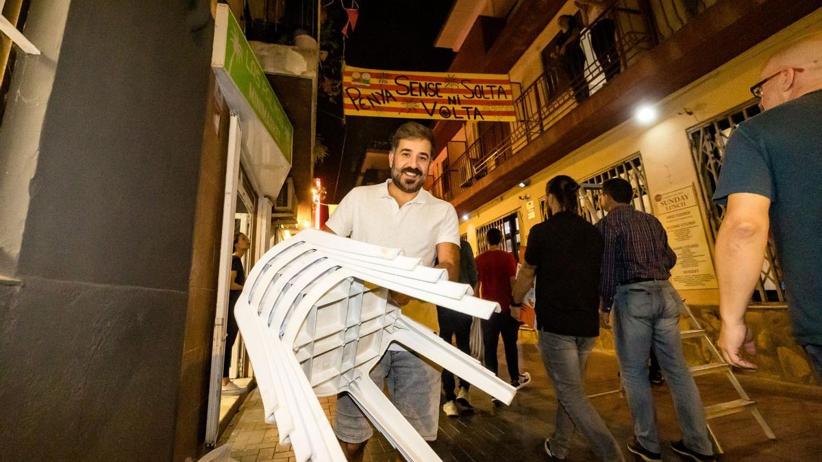 Un festero lleva una pila de sillas hasta el local de su peña, en presencia de otros peñistas.