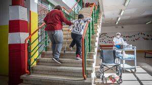 Barreras arquitectónicas en el colegio Frederic Mistral de L’Hospitalet. Un alumno con muletas sube con ayuda la escalera.