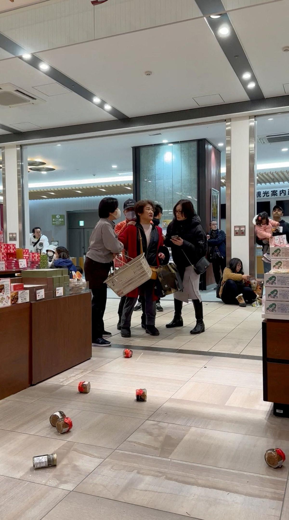 La gente se sienta en el suelo mientras los artículos caen de los estantes en una tienda a causa de un terremoto, en Kanazawa, Ishikawa, Japón